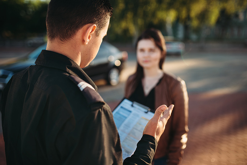 A police officer talks to a woman standing near her car.