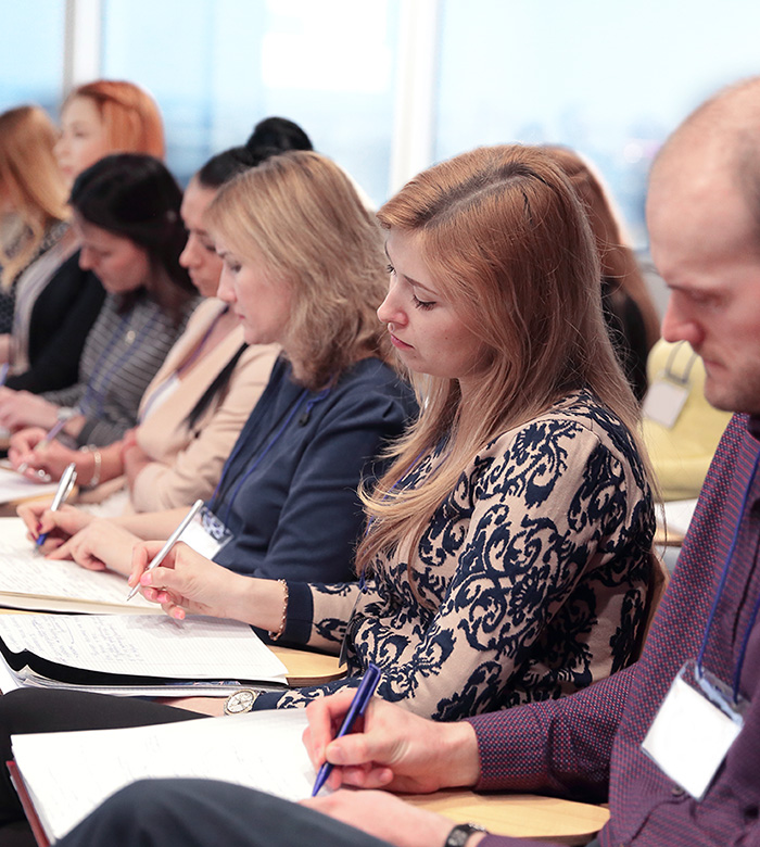 People in the audience at a seminar take notes.