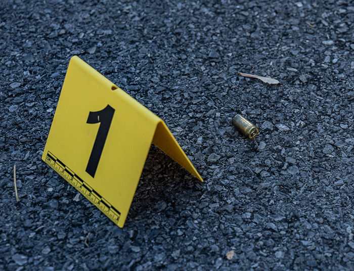 A crime scene evidence market sits beside a bullet casing on asphalt.