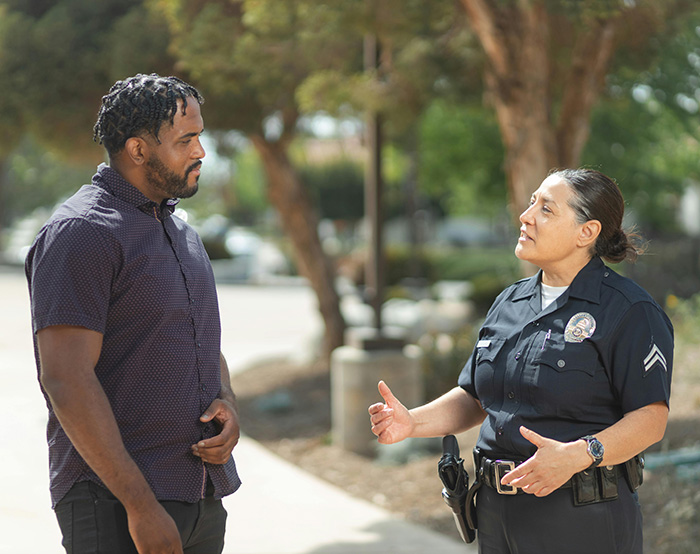 A female police officer and a man have a friendly conversation on a sidewalk.