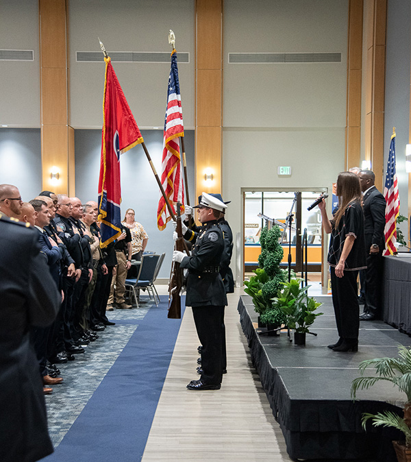 The color guard stands at attention while the national anthem is sung by a woman at a podium.
