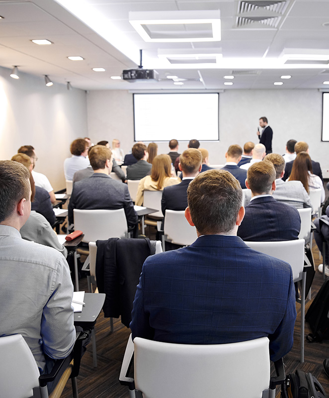 A group of professionals attend a seminar in a large room.