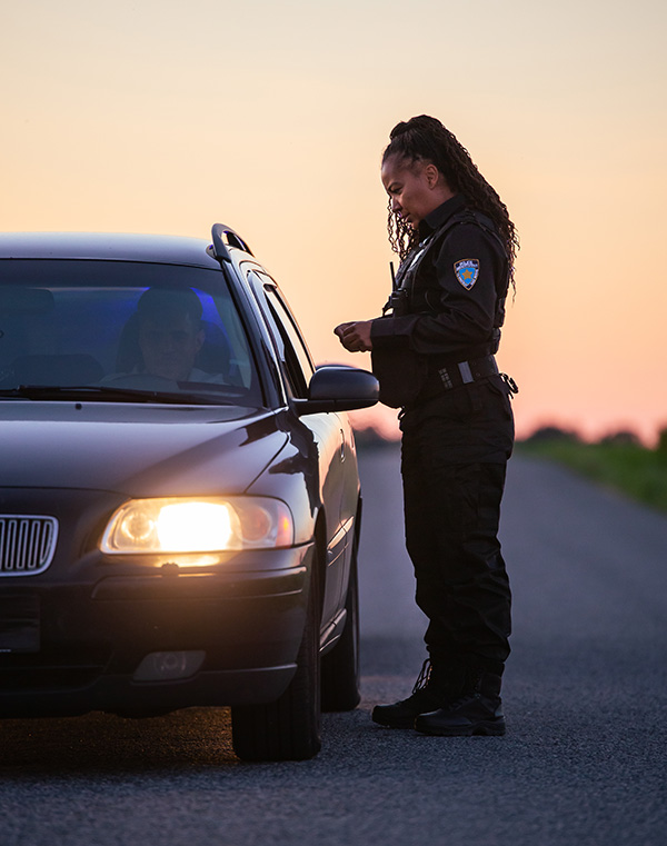 A female police officer talks to a man in a stopped car.