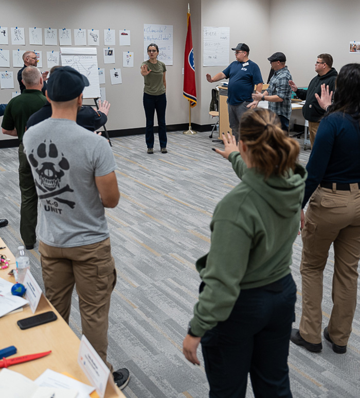 An instructor teaches a room of police officers standing in a circle.